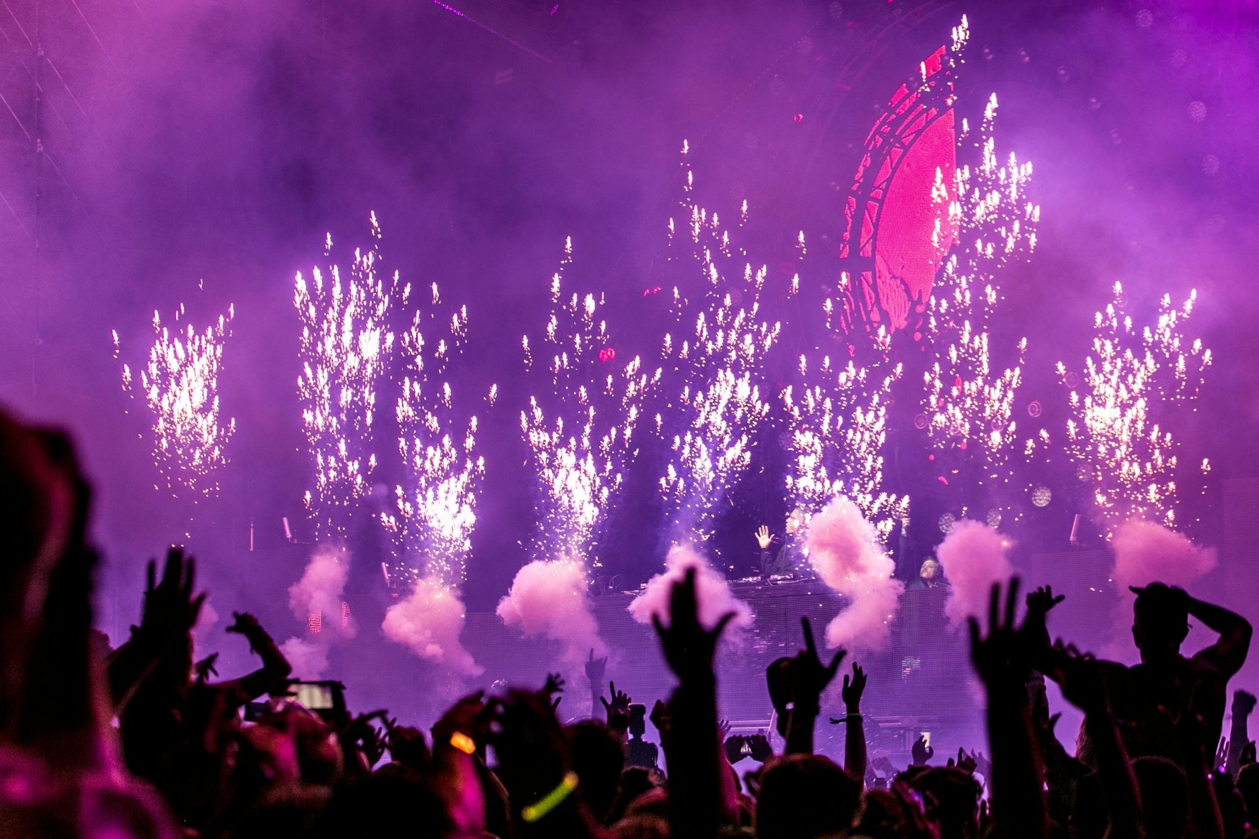 Vibrant EDM concert scene with fireworks, smoke, and enthusiastic crowd enjoying the music.