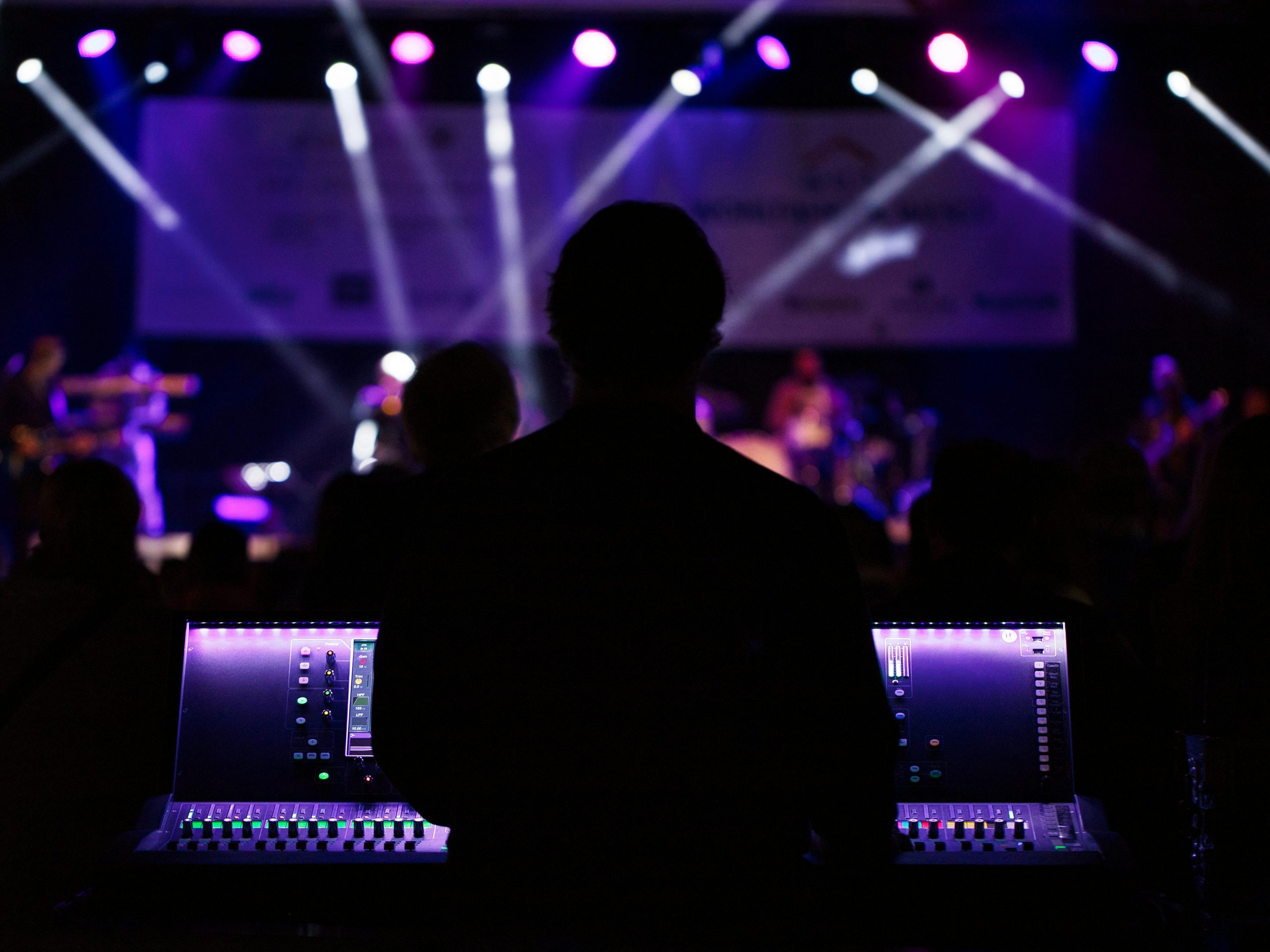 A sound engineer manages the audio mixer during a vibrant live concert with colorful lighting.